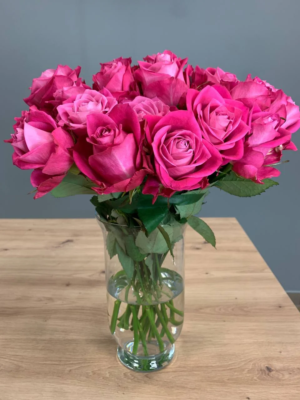 Bukiet różowych róż w szklanym wazonie na drewnianym stole