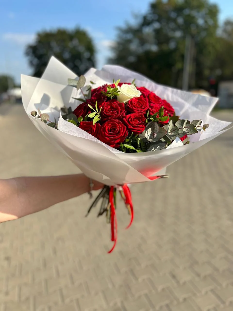Bukiet róż z przewagą czerwonych i pojedynczą białą różą, opakowany w biały papier