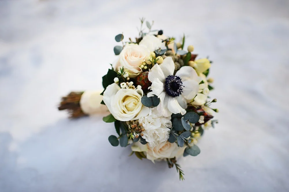 Bukiet ślubny z białych róż i anemonów na tle marmuru